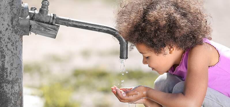 Criança bebe água em bica. Foto: Adobe Stock