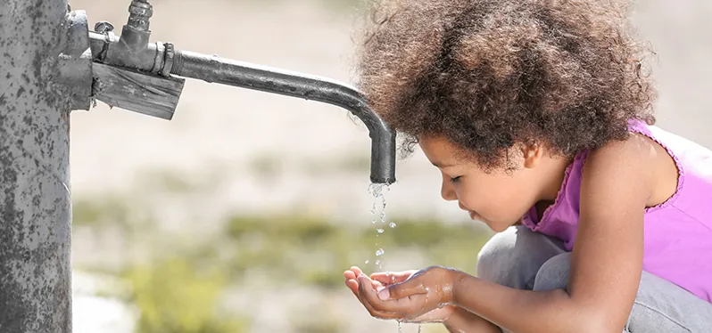 Child drinks water from a spout. Photo: Adobe Stock