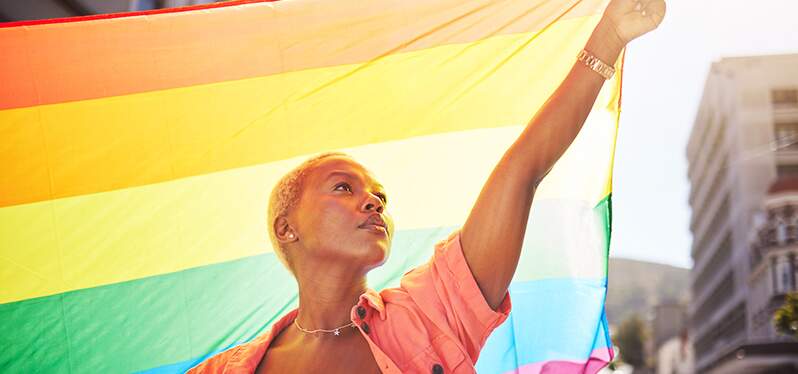 Woman in front of the LGBTQIAP+ flag. Photo: Adobe Stock