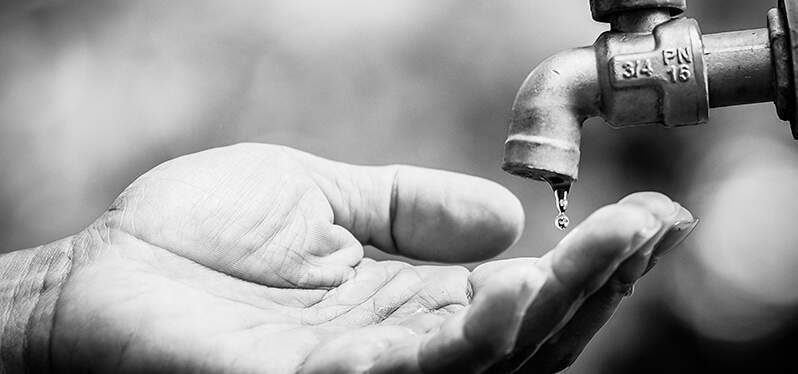 Mano de autosuficiencia de agua debajo del grifo con poca agua corriente Photo-Adobe-Stock