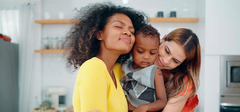 Couple of lesbian women with child on their lap. Photo: Adobe Stock