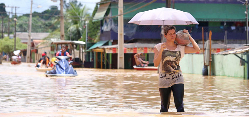 Mulher em meio a uma inundação, um dos recentes desastres naturais. Foto: Agência Brasil