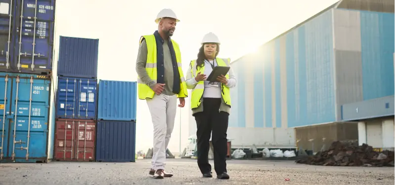 A imagem mostra duas pessoas negras, sendo um homem e uma mulher, trabalhando numa obra